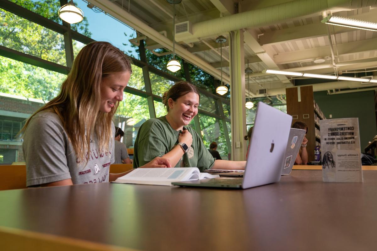 两个学生在图书馆的一张桌子上用笔记本电脑聊天